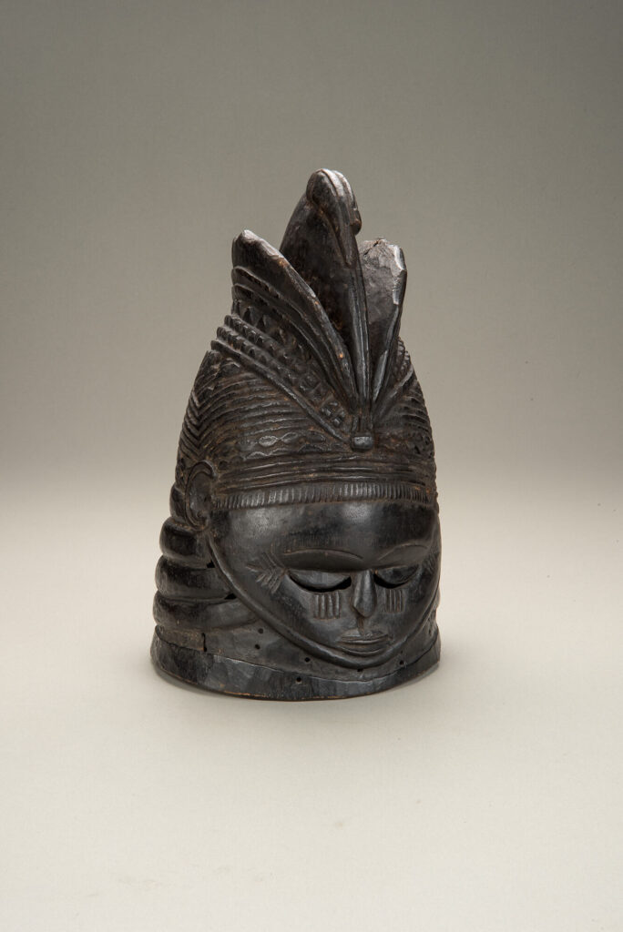 A dark wooden mask with a high forehead, downcast eyes, and small mouth.