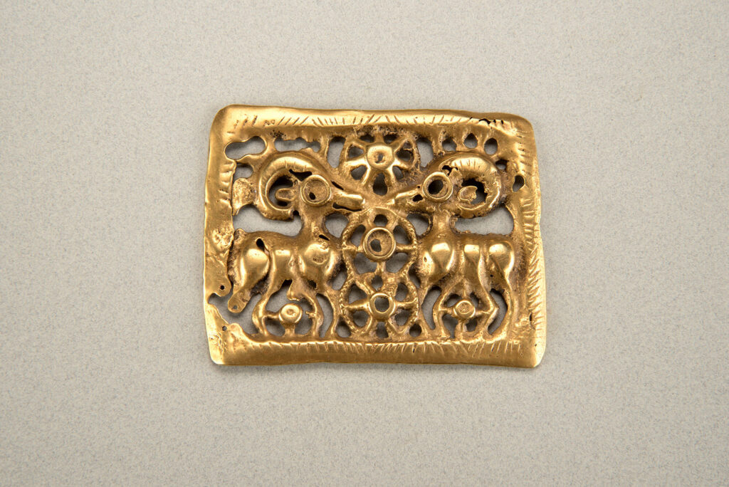 A bronze plaque decorated with two ibexes facing each other, curved horns arching over their backs.