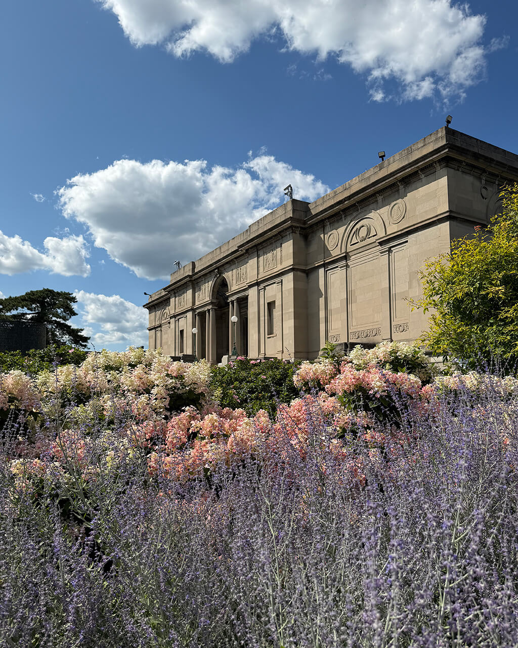 MAG's 1913 museum building on a sunny day, flowers in the foreground.