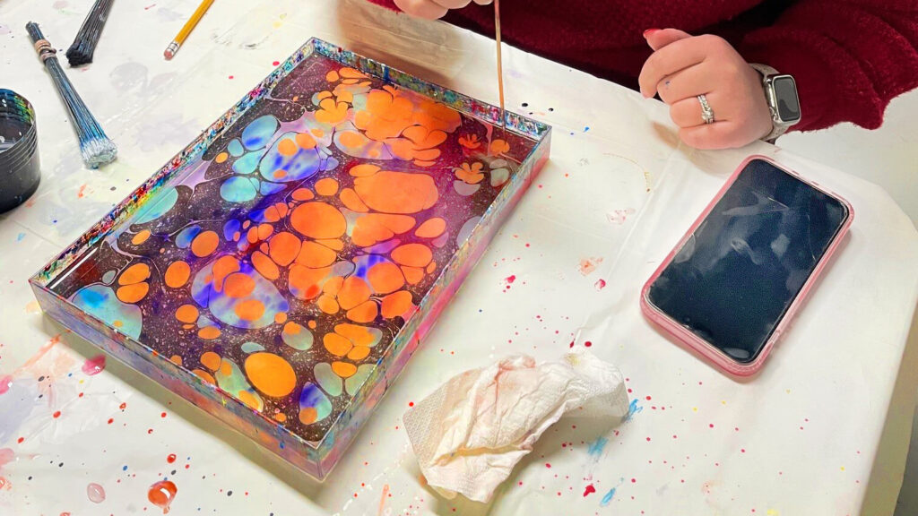 A person creating designs in gold and black paint in a tray for marbling paper.